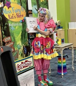 Miss Fairy G performing a magic trick to teach elementary students about kindness during a school assembly show.